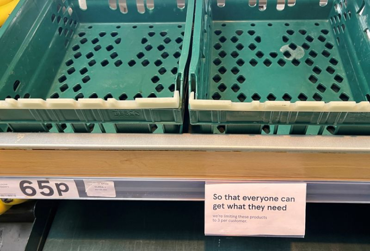 Un panneau limitant les clients à trois articles chacun est visible à côté de boîtes vides dans le rayon des tomates et des poivrons d'un supermarché Tesco à Manchester