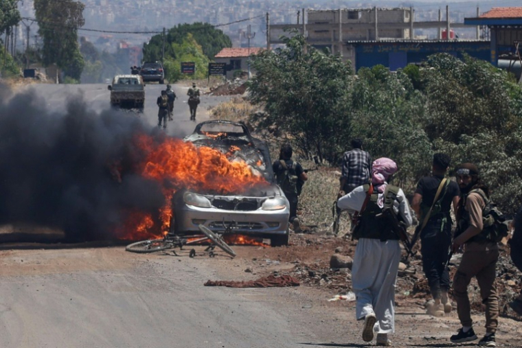 Des combattants bédouins et tribaux se déploient alors qu’une voiture est en feu à l’entrée ouest du bastion druze de Soueïda, dans le sud de la Syrie, le 18 juillet 2025 ( AFP / Bakr ALKASEM )