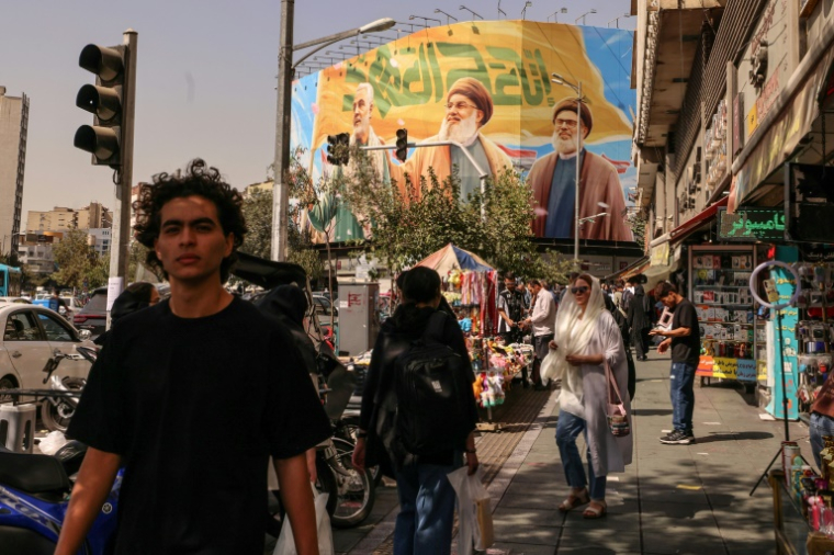 Des passants devant un panneau d'affichage représentant les dirigeants libanais du Hezbollah assassinés Hassan Nasrallah (C) et son successeur Hachem Safieddine (D), ainsi que le général iranien Qassem Soleimani, à Téhéran, le 28 septembre 2025 ( AFP / ATTA KENARE )