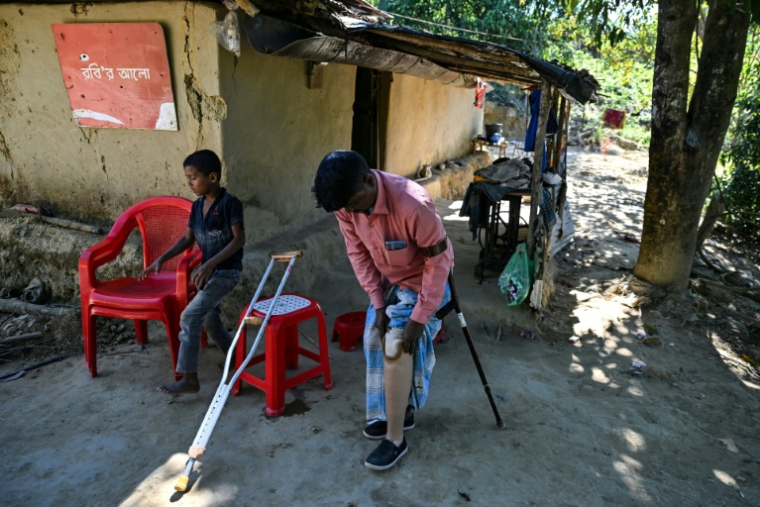 Ali Hossain (à droite), un Bangladais de 40 ans qui a perdu une jambe à cause d’une mine lorsqu'il ramassait du bois, retire sa prothèse devant sa maison dans le district de Bandarban le 19 décembre 2025 ( AFP / Munir UZ ZAMAN )