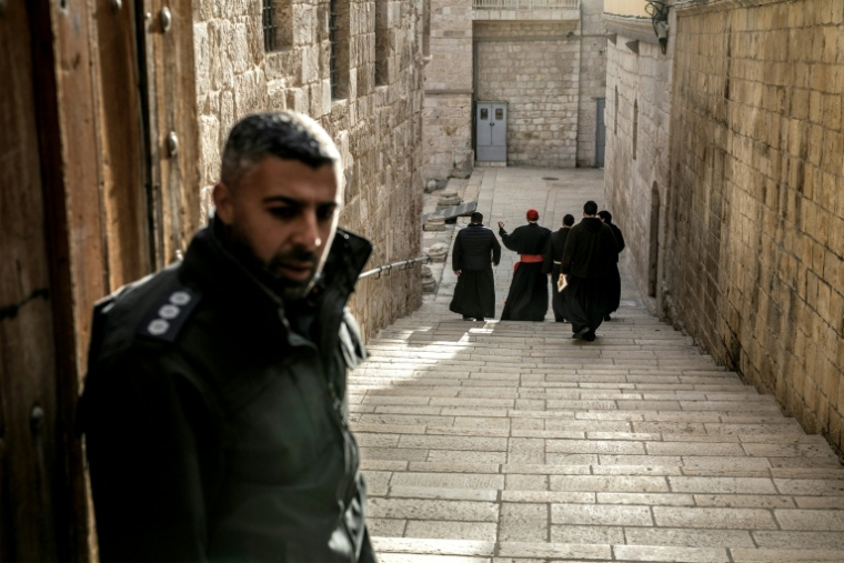 Un policier israélien (à gauche) observe le cardinal Pierbattista Pizzaballa (3e à gauche), patriarche latin de Jérusalem, alors qu'il arrive accompagné d'autres frères franciscains à l'église du Saint-Sépulcre pour la messe du dimanche de Pâques, à huis clos en raison de la guerre en cours, dans la vieille ville de Jérusalem le 5 avril 2026. ( AFP / MARCO LONGARI )