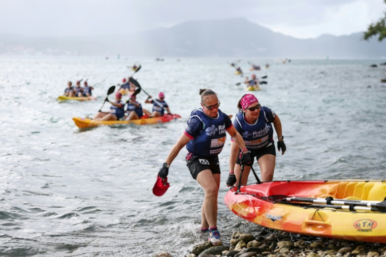 Sonia Latapie (d), souffrant d'insuffisance rénale et atteinte d'un cancer du sein, membre de l'équipe "Les Reines du cœur", porte un kayak avec sa coéquipière Alexia Elineau (d), après avoir participé à une course de kayak du "Raid des Alizés", le 26 novembre 2025 en Martinique ( AFP / Anne-Christine POUJOULAT )
