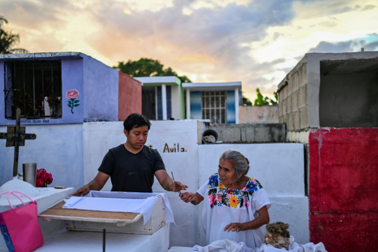 Un jeune accompagné de sa grand-mère se prépare à nettoyer les restes d'un proche avant les célébrations du Jour des Morts au cimetière de Pomuch, dans l'État de Campeche, au Mexique, le 18 octobre 202 ( AFP / Yuri CORTEZ )