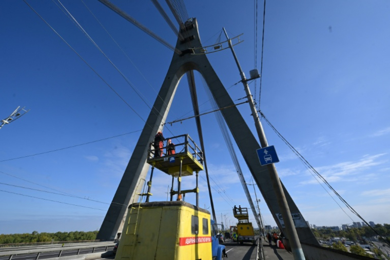 Des techniciens réparent une ligne électrique de trolleybus à proximité des dégâts constatés sur un pilier du pont, à la suite d’une attaque de drone contre le pont du Nord à Kiev, le 3 octobre 2026 ( AFP / Sergei SUPINSKY )