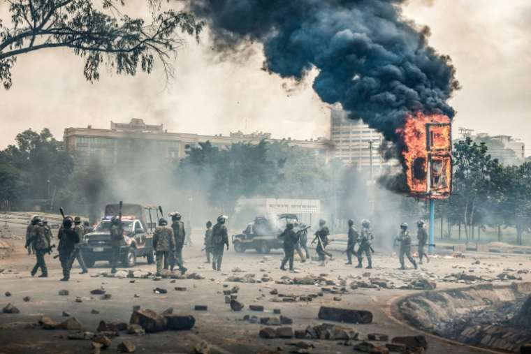 Des membres des forces de sécurité près d'un panneau publicitaire en feu après des heurts avc des manifestants lors des commémorations du premier anniversaire de la prise du Parlement, le 25 juin 2025 à Nairobi, au Kenya ( AFP / Luis TATO )