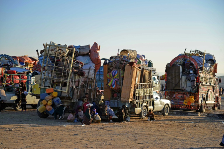 Des réfugiés afghans assis à côté des camions dans un centre d'enregistrement, à leur arrivée du Pakistan, dans le district de Takhta Pul de la province de Kandahar,  le 18 décembre 2023 ( AFP / Sanaullah SEIAM )