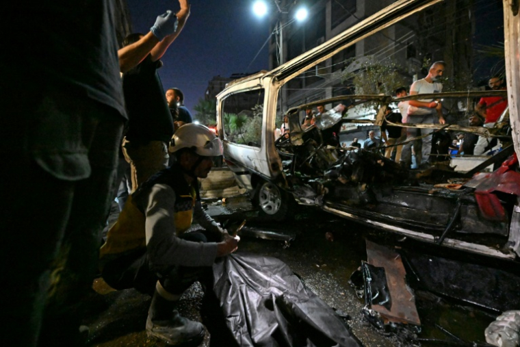 Des passants et des secouristes inspectent la carcasse du minibus dans lequel une bombe a explosé, à Jaramana, près de la capitale syrienne, Damas, le 6 août 2026 ( AFP / LOUAI BESHARA )