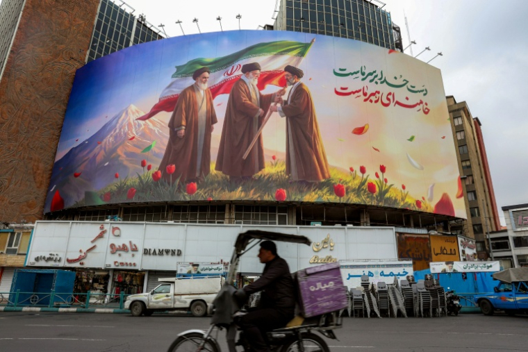 Un homme en deux-roues circule devant une affiche montrant l'ayatollah Ali Khamenei tendant le drapeau iranien à son fils l'ayatollah Mojtada Khamenei, nouveau guide suprême, sous le regard de l'ayatollah Rouhollah Khomeini, fondateur de la République islamique, le 11 mars à Téhéran ( AFP / - )