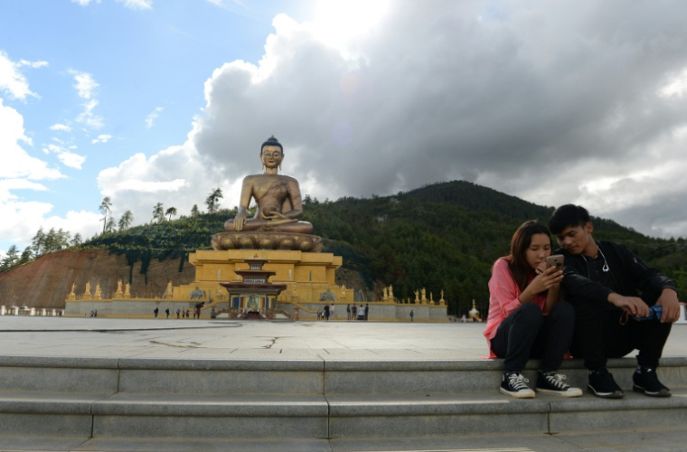 Un couple assis regarde l'écran d'un téléphone portable à côté d'une statue de Bouddha à Thimphou, la capitale du Bouthan, le  25 août 2018 ( AFP / ARUN SANKAR )