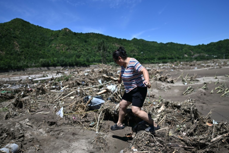 Une femme passe devant une zone endommagée par les pluies dans le district de Huairou, à la périphérie de Pékin, le 30 juillet 2025 ( AFP / Pedro Pardo )