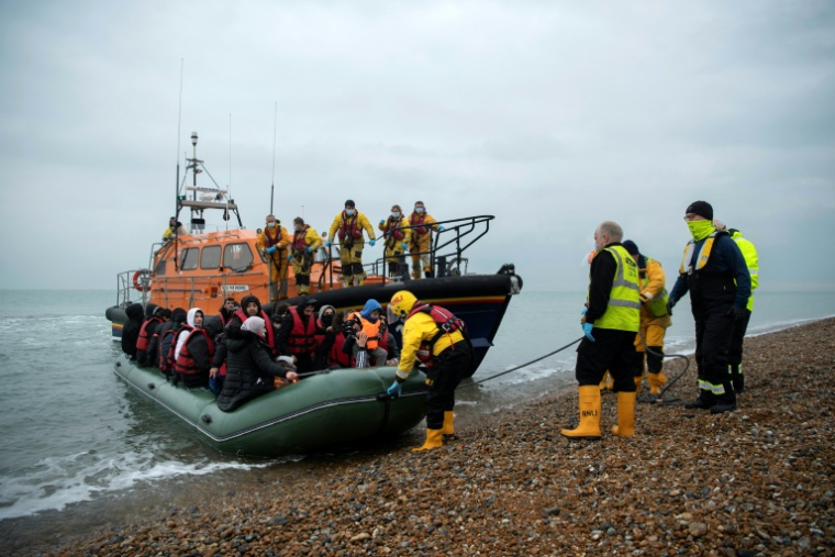 Des migrants sont aidés à débarquer d'un canot de sauvetage de la RNLI (Royal National Lifeboat Institution) sur une plage de Dungeness, en Angleterre, le 24 novembre 2021, après avoir été secourus alors qu'ils traversaient la Manche ( AFP / Ben STANSALL )