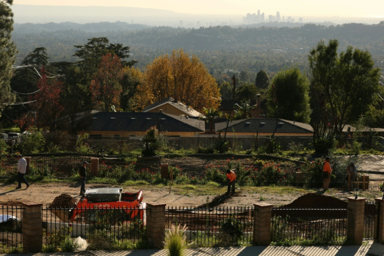 Des ouvriers creusent les fondations d'une maison à Altadena, avec à l'horizon les tours du centre-ville de Los Angeles, le 29 décembre 2025  ( AFP / Patrick T. Fallon )
