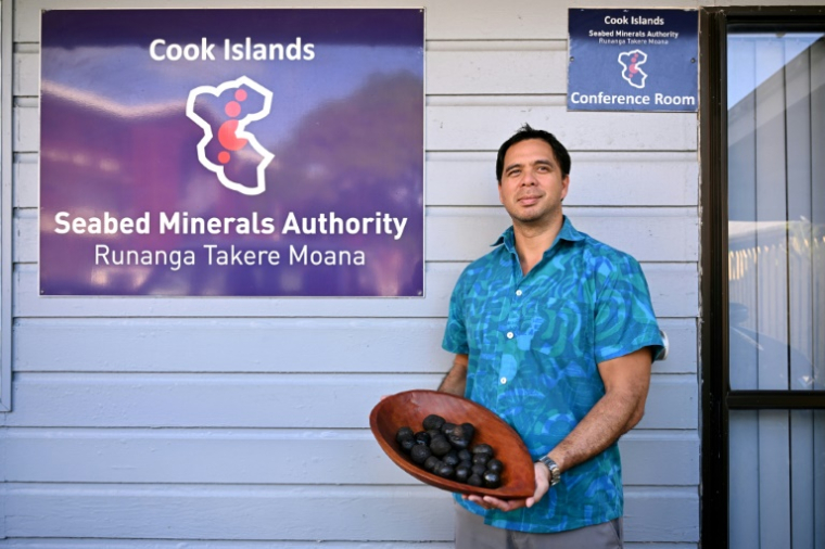 Edward Herman, de l'Autorité des minéraux des fonds marins des îles Cook, montre ds globes noirs incrustés de cobalt, de nickel, de manganèse et d'autres métaux convoités lors d'une interview avec l'AFP, le 12 juin 2025 à Rarotonga, aux îles Cook ( AFP / William WEST )