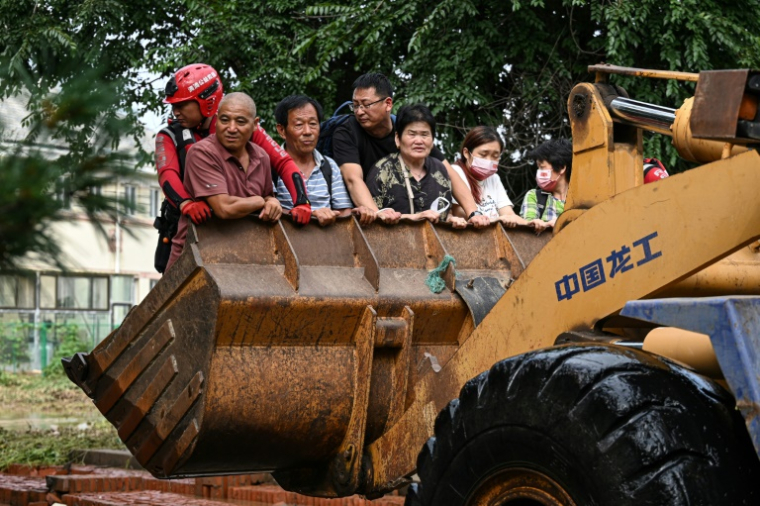 Des habitants empruntent un chargeur frontal pour traverser une rue inondée après de fortes pluies dans le village de Taishitun, dans le district de Miyun, à la périphérie de Pékin, le 28 juillet 2025 ( AFP / Jade GAO )
