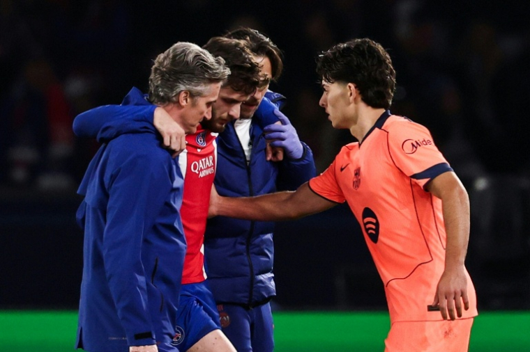 L'attaquant du PSG Khvicha Kvaratskhelia (c) quitte la pelouse après s'être blessé au genou droit lors du match contre le FC Barcelone, réconforté par Xavi Espart, le 20 octobre 2026 au Parc des Princes ( AFP / FRANCK FIFE )