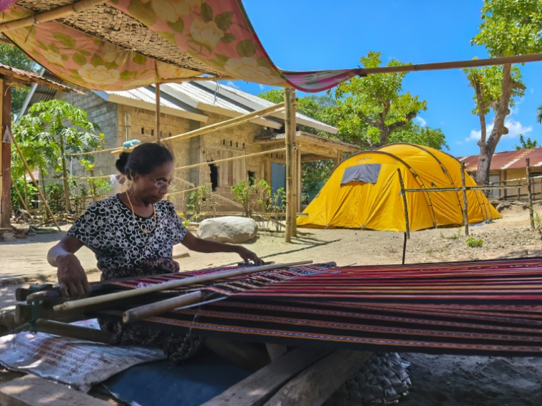 Une femme tisse à l'extérieur de sa maison endommagée par un séisme de magnitude 7,7 survenu le 15 août, dans le village de Meken Detun, là Sikka, e 14 septembre 2026 en Indonésie ( AFP / ARNOLD WELIANTO )