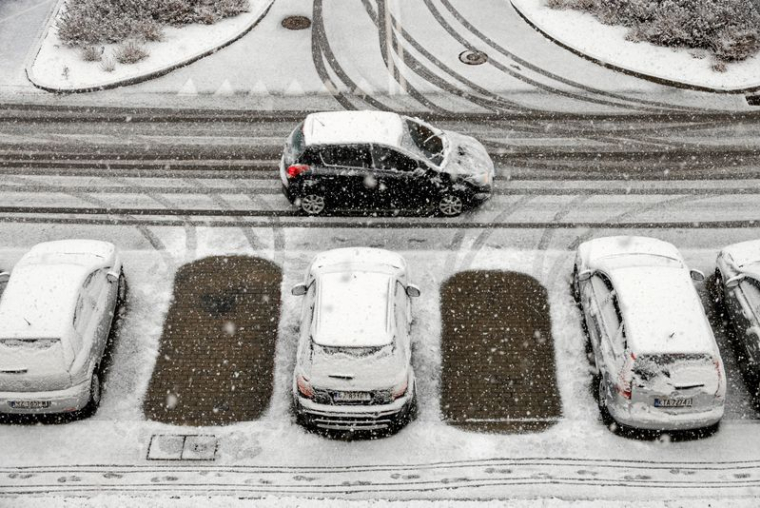 Une voiture passe devant des voitures couvertes de neige garées sur un parking après des chutes de neige à Rzeszow