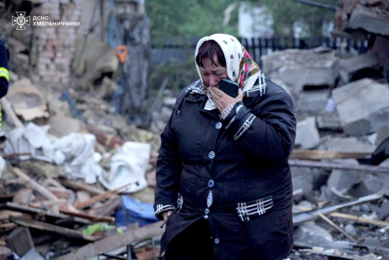 Photo prise et diffusée par le service de presse des services d'urgence de l'État ukrainien, le 25 mai 2025, montrant une femme en larmes à côté de sa maison endommagée par une frappe russe dans la région Khmelnytskyi, dans l'ouest du pays ( Service de presse des services d'urgence de l'État ukrainien / Handout )
