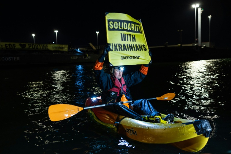Un militant de Greenpeace brandit une affichette lors d'une action pour dénoncer le commerce d'uranium entre la Russie et la France le 2 mars 2026 dans le port de Dunkerque ( AFP / Sameer Al-DOUMY )