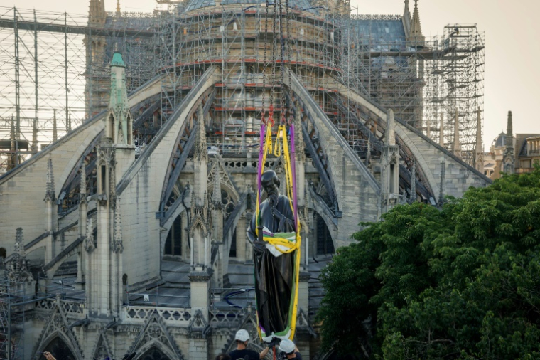 Une grue soulève l'une des 16 statues géantes d'apôtres pour la replacer sur sa base au pied de la flèche de la cathédrale Notre-Dame de Paris, le 23 juin 2025 ( AFP / GEOFFROY VAN DER HASSELT )