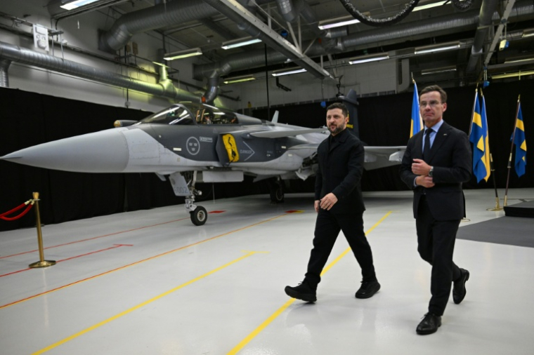 Le Premier ministre suédois Ulf Kristersson (d) et le président ukrainien Volodymyr Zelensky passent devant un avion de chasse Gripen à l'issue d'une conférence de presse conjointe à Linköping, en Suède, le 22 octobre 2025 ( AFP / Jonathan Nackstrand )