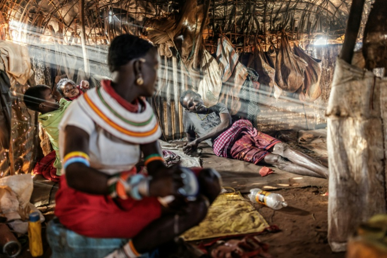 Le pasteur samburu Chapan Lolpusike (allongé) parle avec sa femme Soilin Lolpusike (au premier plan), dans leur hutte près de Sereolipi (Kenya), le 29 septembre 2025 ( AFP / Luis TATO )