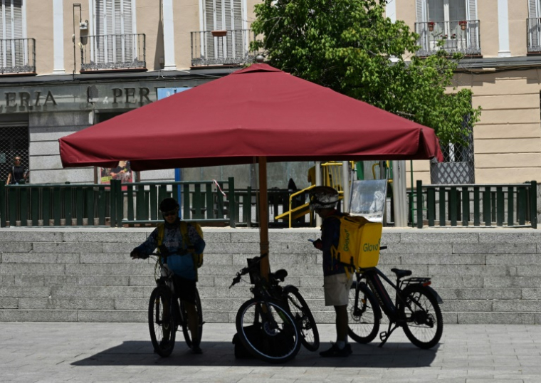Des livreurs s'abritent du soleil sous un parasol à Madrid, le 18 juin 2025 lors d'une vague de chaleur en Espagne ( AFP / JAVIER SORIANO )