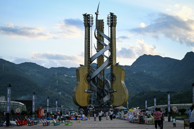Cette photo prise le 26 juillet 2026 montre des passants devant une immense installation de guitares sur la place de la Culture de la guitare à Zheng'an, dans la province du Guizhou, dans le sud-ouest de la Chine. ( AFP / Jade GAO )