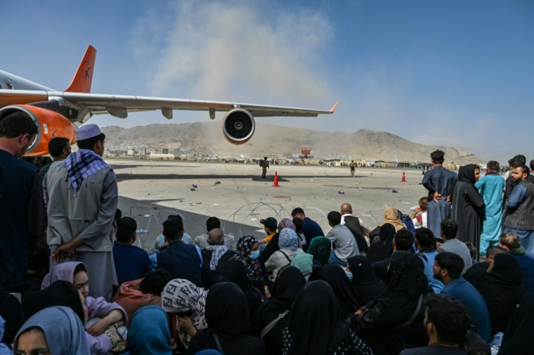 Des Afghans assis sur le tarmac de l'aéroport de Kaboul pris d'assaut dans l'espoir d'une évacuation après la reprise de la capitale par les talibans, le 16 août 2021  ( AFP / Wakil Kohsar )