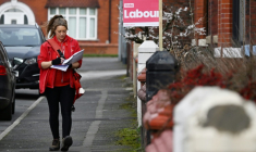 Une postière passse devant une affiche pour le Parti travailliste dans une rue résidentielle de Denton, dans le Grand Manchester, au nord-ouest de l'Angleterre, le 25 février 2026, la veille de l'élection législative partielle cruciale de Gorton et Denton.  ( AFP / Paul ELLIS )