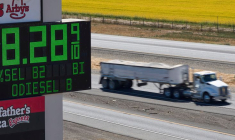 Des poids lourds passent devant un panneau indiquant les prix du carburant