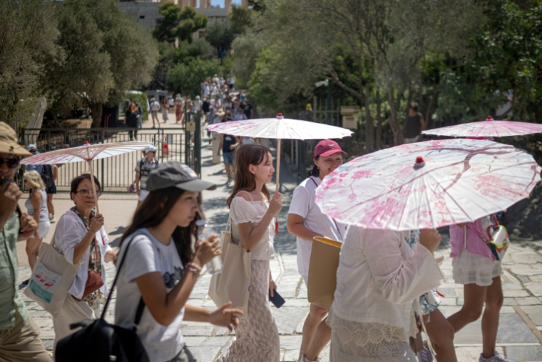 Des touristes, qui attendent pour accéder au site de l'Acropole, se protègent du soleil avec des ombrelles, le 1er juillet 2025 à Athènes ( AFP / Angelos TZORTZINIS )