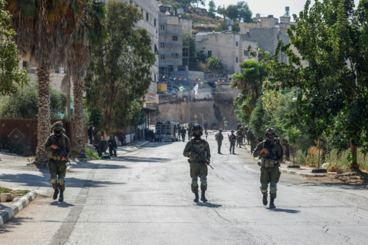 Des soldats israéliens patrouillent dans une rue de Qusra, en Cisjordanie occupée, où des colons israéliens assiègent des maisons palestiniennes, le 13 août 2026 ( AFP / Zain JAAFAR )