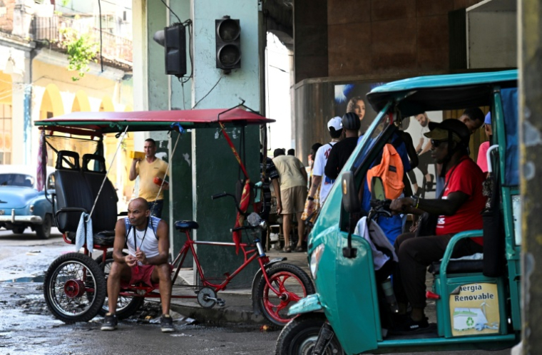 Un véhicule passe devant un feu de signalisation éteint pendant une coupure de courant, tandis qu'un homme est assis sur son tricycle à La Havane, le 10 septembre 2025 ( AFP / YAMIL LAGE )