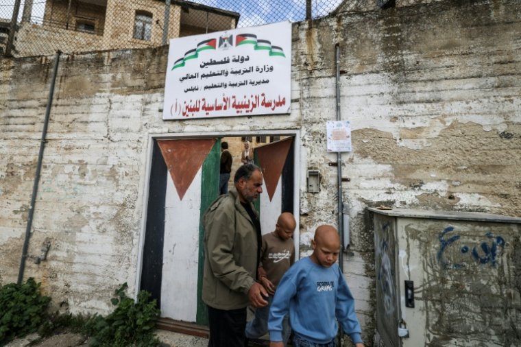 Les jumeaux Ahmad (d) et Mohammad, accompagnés par leur père Ibrahim al-Hajj, sortent de leur école à Naplouse, le 10 février 2026 en Cisjordanie occupée ( AFP / Jaafar ASHTIYEH )