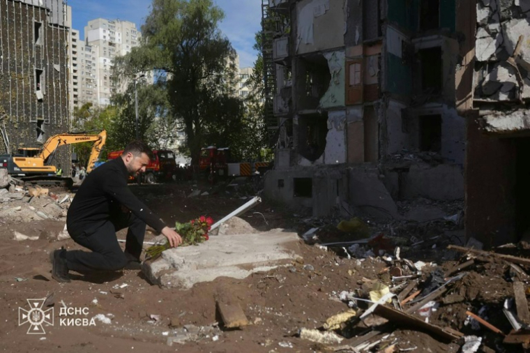 Photo prise et diffusée par les services d'urgence ukrainiens, le 15 mai 2026, montrant le président ukrainien Volodymyr Zelensky déposant des fleurs sur le site d'une attaque aérienne à Kiev ( UKRAINIAN EMERGENCY SERVICE / Handout )