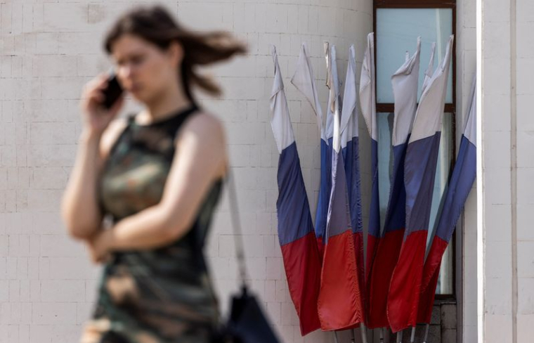 Une femme parle au téléphone en passant devant des drapeaux nationaux russes à Koursk
