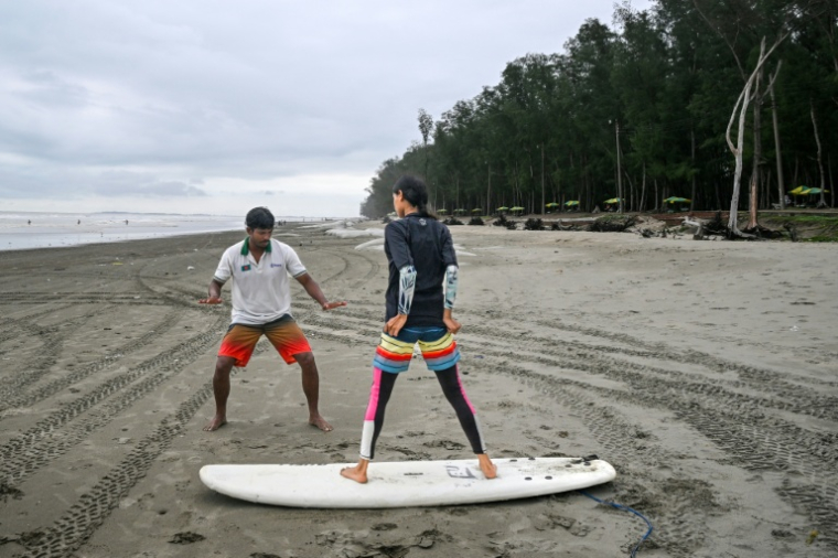 Mohammad Mannan (G) donne un cours de surf à un débutant, sur la plage de Cox's Bazar, dans le sud-est du Bangladesh, le 22 juin 2026   ( AFP / Munir UZ ZAMAN )