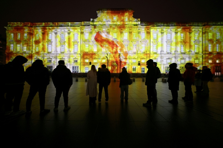 Des passants devant le palais Saint-Pierre illuminé avec "Le Lundi c’est Raviolis" de l'artiste Tigrelab durant l'avant première de la Fête des lumières à Lyon, le 4 décembre 2025 ( AFP / Alex MARTIN )