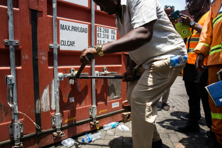 Un membre de l'unité de lutte contre la criminalité organisée transnationale ouvre l’un des quatre conteneurs saisis contenant des comprimés et des gélules de tapentadol en provenance d’Inde, au terminal de Freetown, le 27 mars 2026 en Sierra Leone  ( AFP / Saidu BAH )