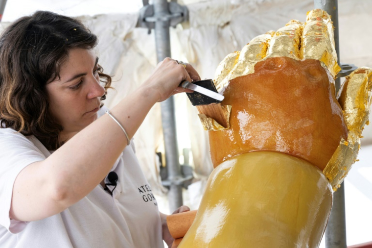 La restauratrice d'art Cyrielle D'Antoni travaille avec des feuilles d'or sur la statue de Jésus, à côté de la Vierge Marie, lors de la rénovation de la basilique Notre-Dame de la Garde à Marseille, le 3 septembre 2025 ( AFP / Miguel MEDINA )