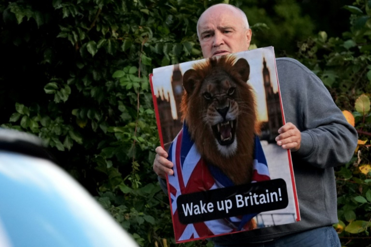 Un manifestant tient une pancarte devant l'hôtel Bell hébergeant des demandeurs d'asile, le 29 août 2025 à Epping, au nord de Londres ( AFP / CARLOS JASSO )