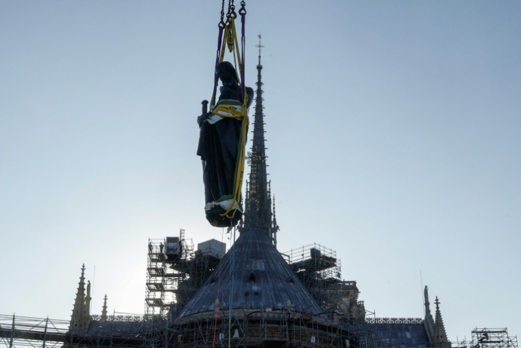 Une grue soulève l'une des 16 statues géantes d'apôtres pour la replacer sur sa base au pied de la flèche de la cathédrale Notre-Dame de Paris, le 23 juin 2025 ( AFP / GEOFFROY VAN DER HASSELT )
