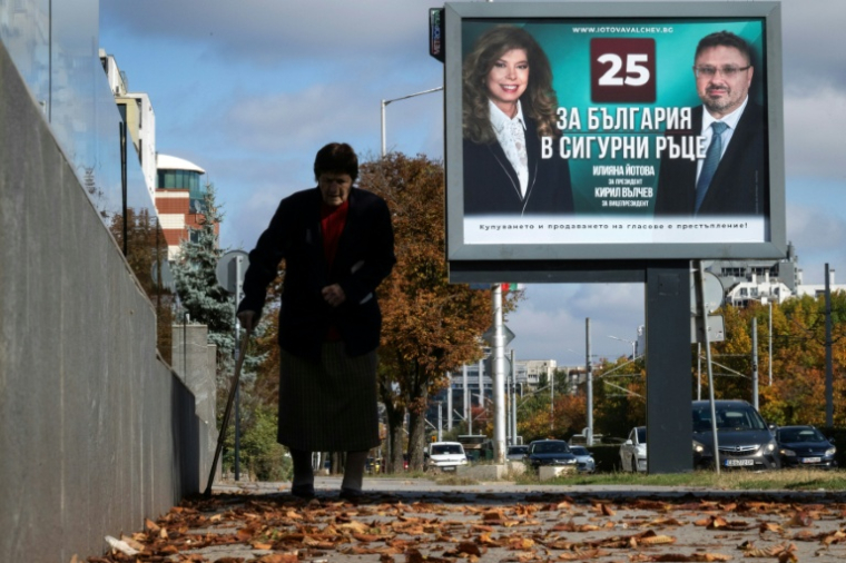 Une personne marche devant une affiche électorale de la présidente sortante de Bulgarie, Iliana Iotova, et de son vice-président candidat Kiril Valchev, à Sofia, le 23 octobre 2026 ( AFP / Nikolay DOYCHINOV )