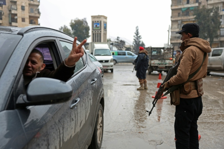 Un conducteur fait le V de la victoire en passant devant un membre des forces de syriennes, après la prise de contrôle par l'armée des quartiers kurdes d'Alep à l'issue de plusieurs jours de combats, le 11 janvier 2026 ( AFP / OMAR HAJ KADOUR )