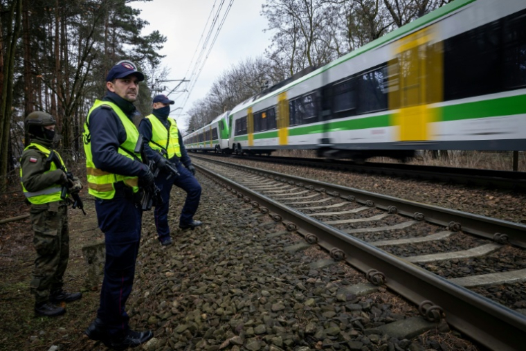 Des gardes de la sécurité ferroviaire armés et un soldat des Forces de défense territoriale patrouillent le long des voies ferrées dans la banlieue de Varsovie, le 27 novembre 2025 en Pologne ( AFP / Wojtek RADWANSKI )