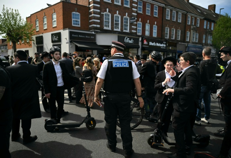 Un officier de la Metropolitan Police demande à des membres de la communauté juive de s'éloigner d'un cordon à l'angle de Golders Green Road et Beverley Gardens, dans le quartier de Golders Green, au nord de Londres, le 29 avril 2026 ( AFP / JUSTIN TALLIS )