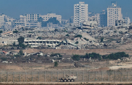 Un véhicule blindé de transport de troupes manœuvre le long du côté israélien de la frontière, tandis que la destruction à Gaza est visible
