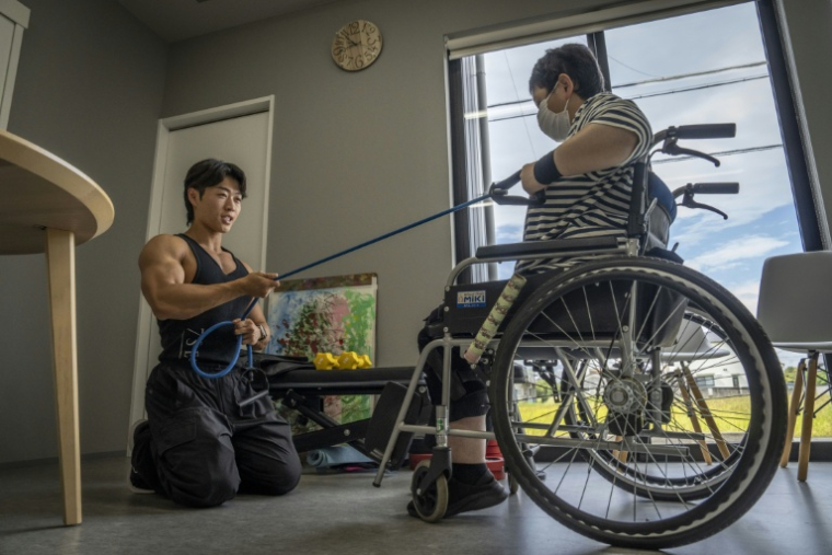 Hokuto Tatsumi (g), auxiliaire de vie et culturiste, aide une patiente (d) à s'entraîner dans un foyer pour personnes handicapées géré par Visionary à Ichinomiya, au Japon, le 29 septembre 2025 ( AFP / Yuichi YAMAZAKI )