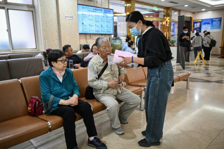 Meng Jia (d), une accompagnatrice de patient, prend en charge Gao Yingmin (g) et Tian Yigui (c) pour les guider dans un hôpital à Pékin, le 22 mai 2025 ( AFP / Jade GAO )